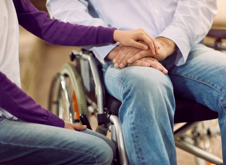 Splecione dłonie niepełnosprawnego i opiekuna. Obrazek w tekście: Formy pomocy osobom niepełnosprawnym: Praktyczny przewodnik