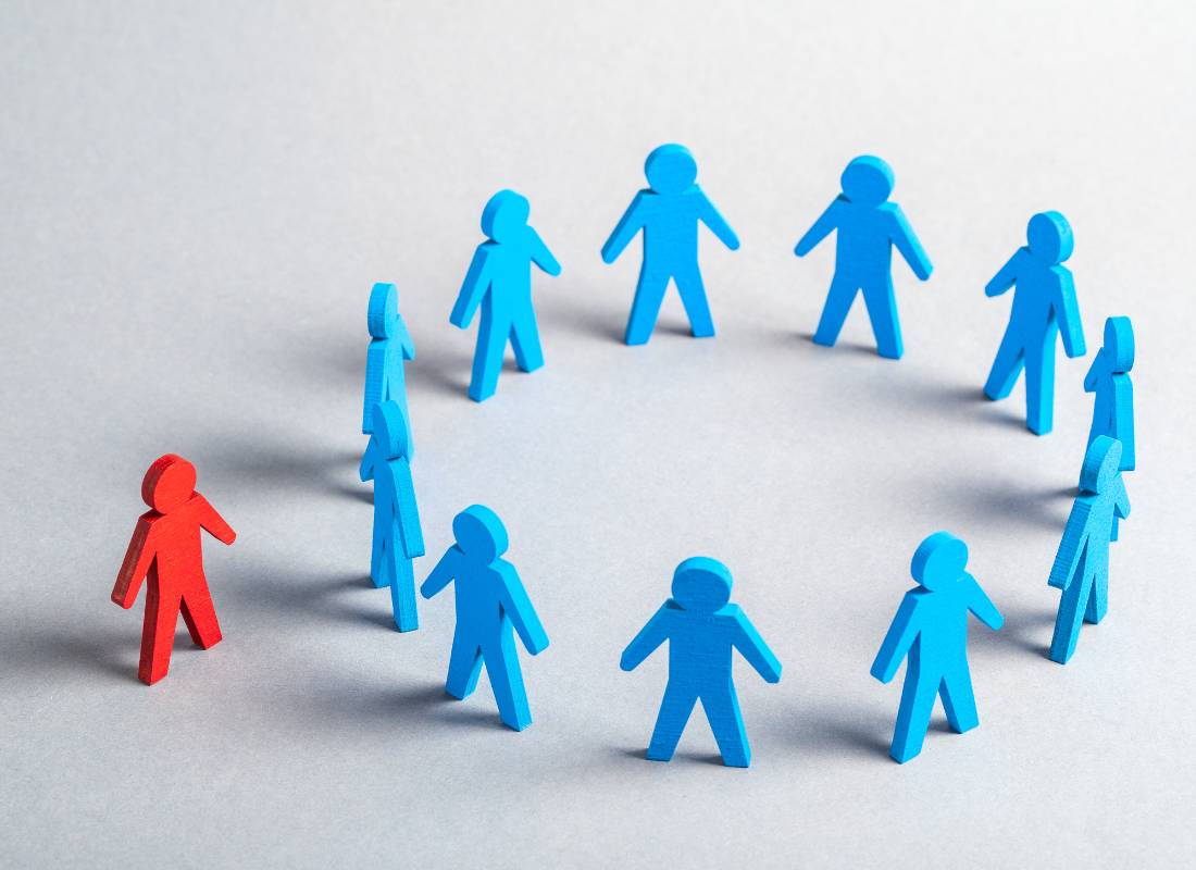 Grafika: krąg niebieskich sylwetek, a poza nim czerwona sylwetka. Obrazek z artykułu: Skąd się biorą uprzedzenia? Przyczyny i konsekwencje